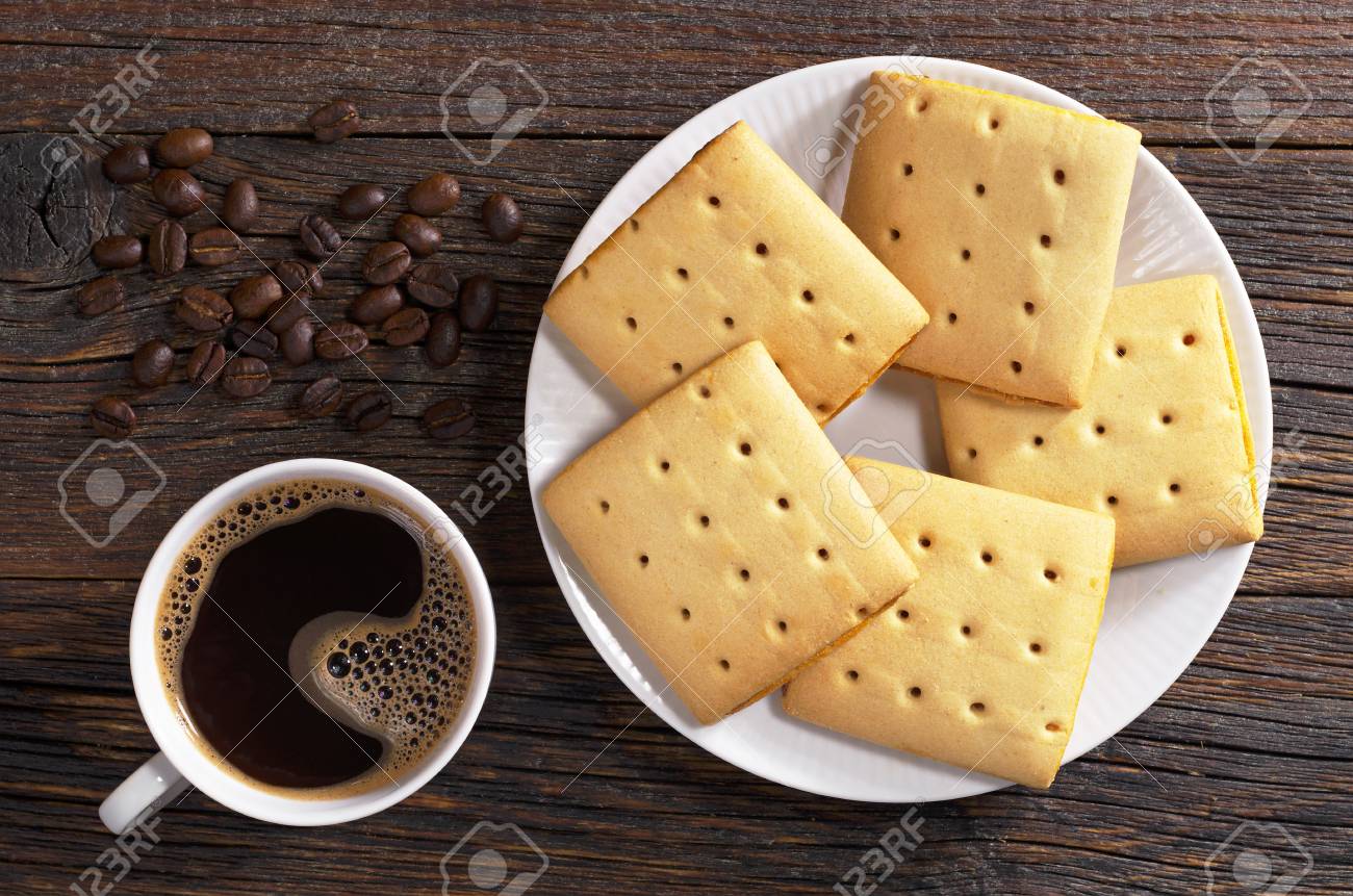 84566105-taza-de-café-caliente-y-galletas-cuadradas-con-mermelada-en-la-placa-en-la-mesa-de-ma...jpg