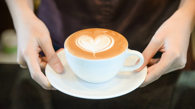 mujer-sirviendo-cafe-mientras-pie-cafeteria-concentrese-taza-forma-corazon-latte-art-manos-fem...jpg